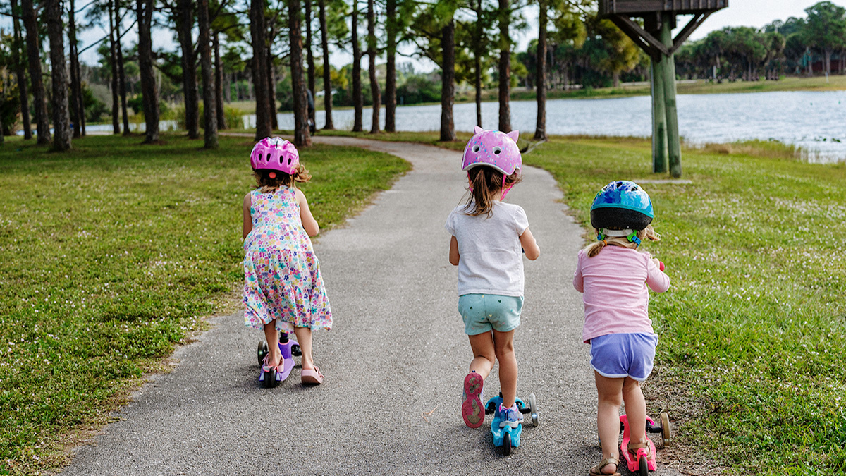 Three young children using scooters Three young children using scooters in a park wearing safety helmets