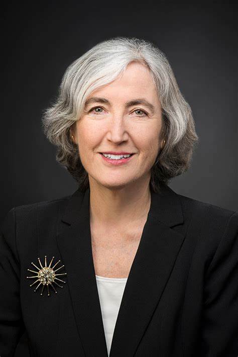 White woman with gray hair, wearing black suit jacket, smiling at camera