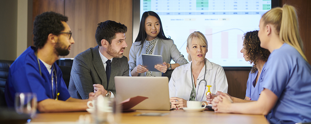 How to Implement ELR Team meeting between various staff members including physicians, patient care team, and hospital administration showing graphs with data on a screen in background.
