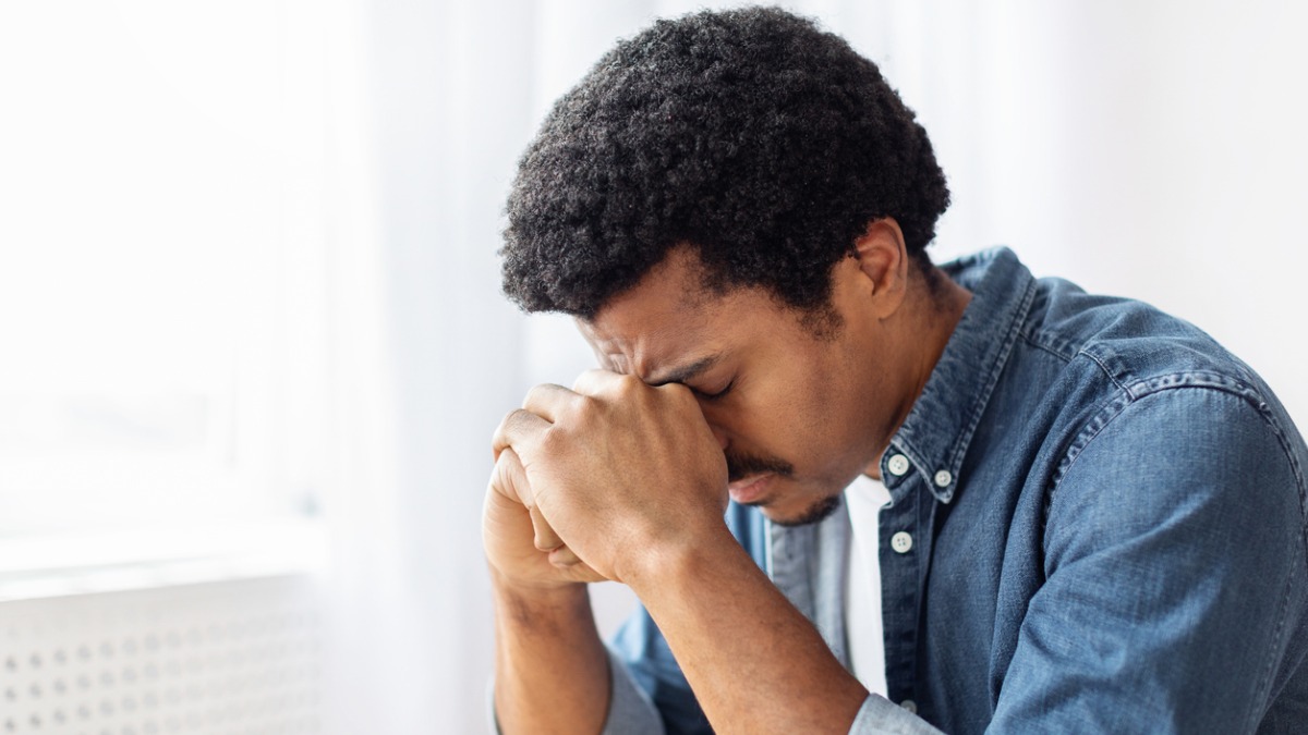 Young Black Man Head in Hands Image of young, black man expressing frustration with managing difficult emotions and rubbing his forehead.
