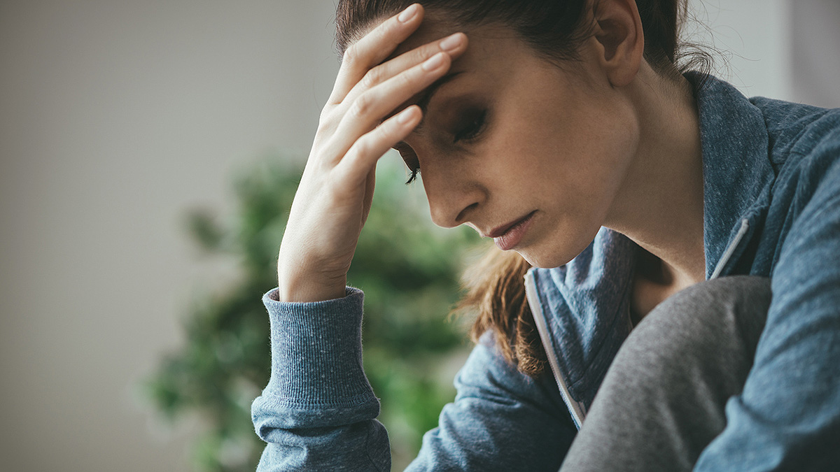 Well-Being Woman Holding Forehead Sad woman bent over holding her forehead in her hand.