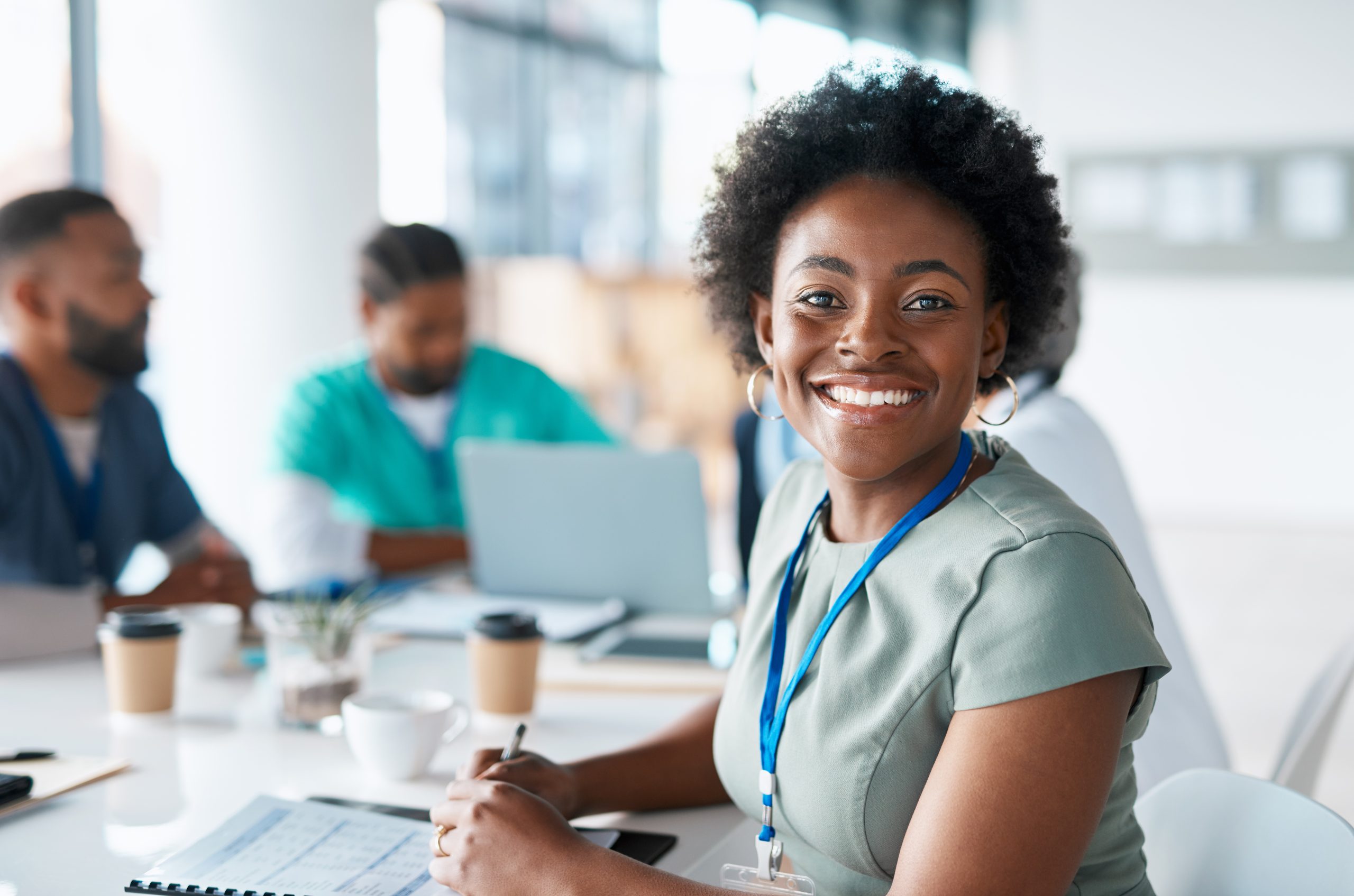 Health Department Staff Young black woman looking at the camera, sitting at a table with other public health colleagues.