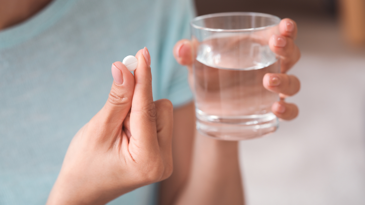 Vitamin Intake Focused view of a small, white vitamin tablet and glass of water in a person's hand