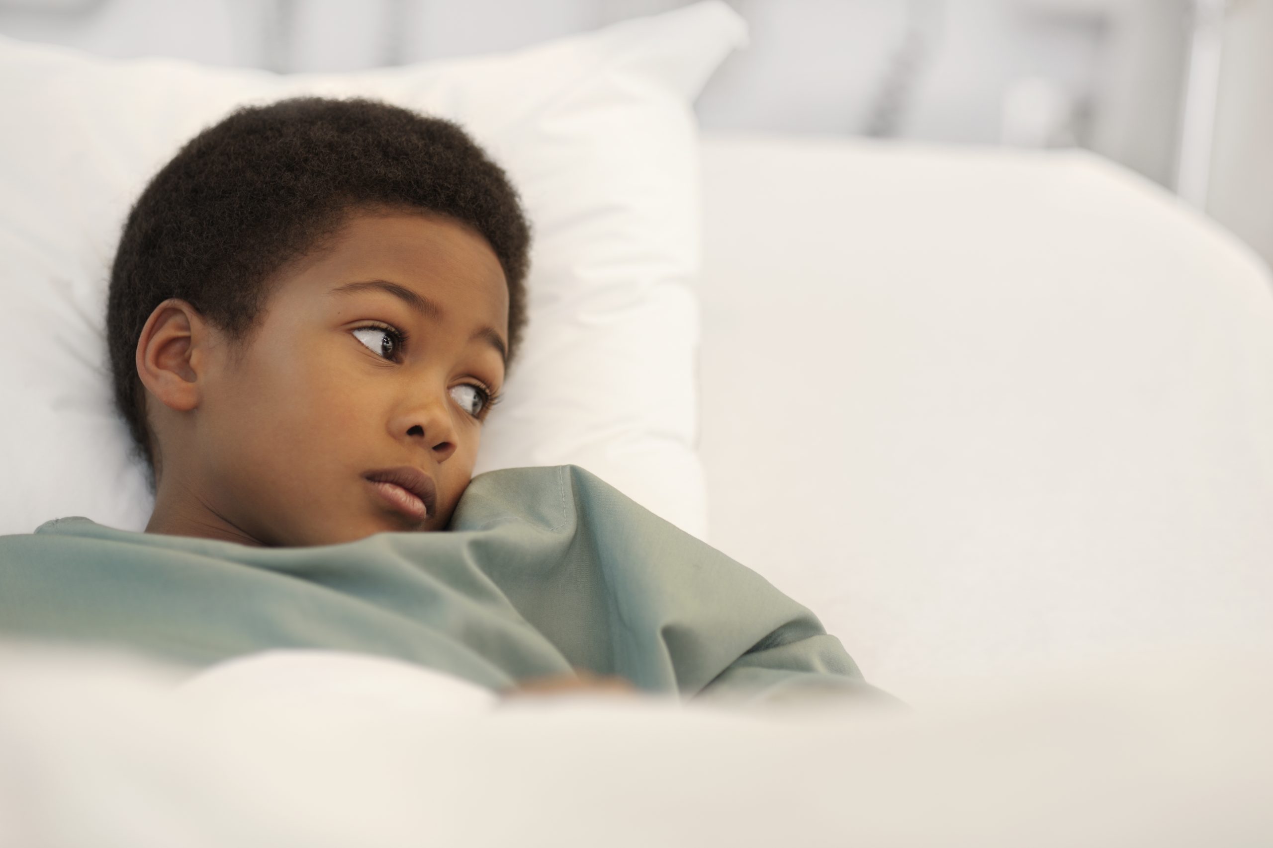 A sick boy laying in a hospital bed, looking to the side.