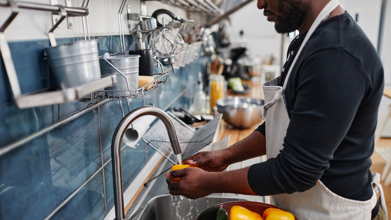 — title missing — Man in commercial kitchen washing vegetables.