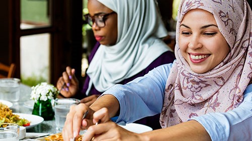 Cultural food preferences Two Muslim women in traditional attire dining in a worksite cafeteria.