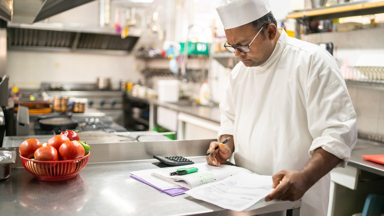 — title missing — Chef with papers in commercial kitchen