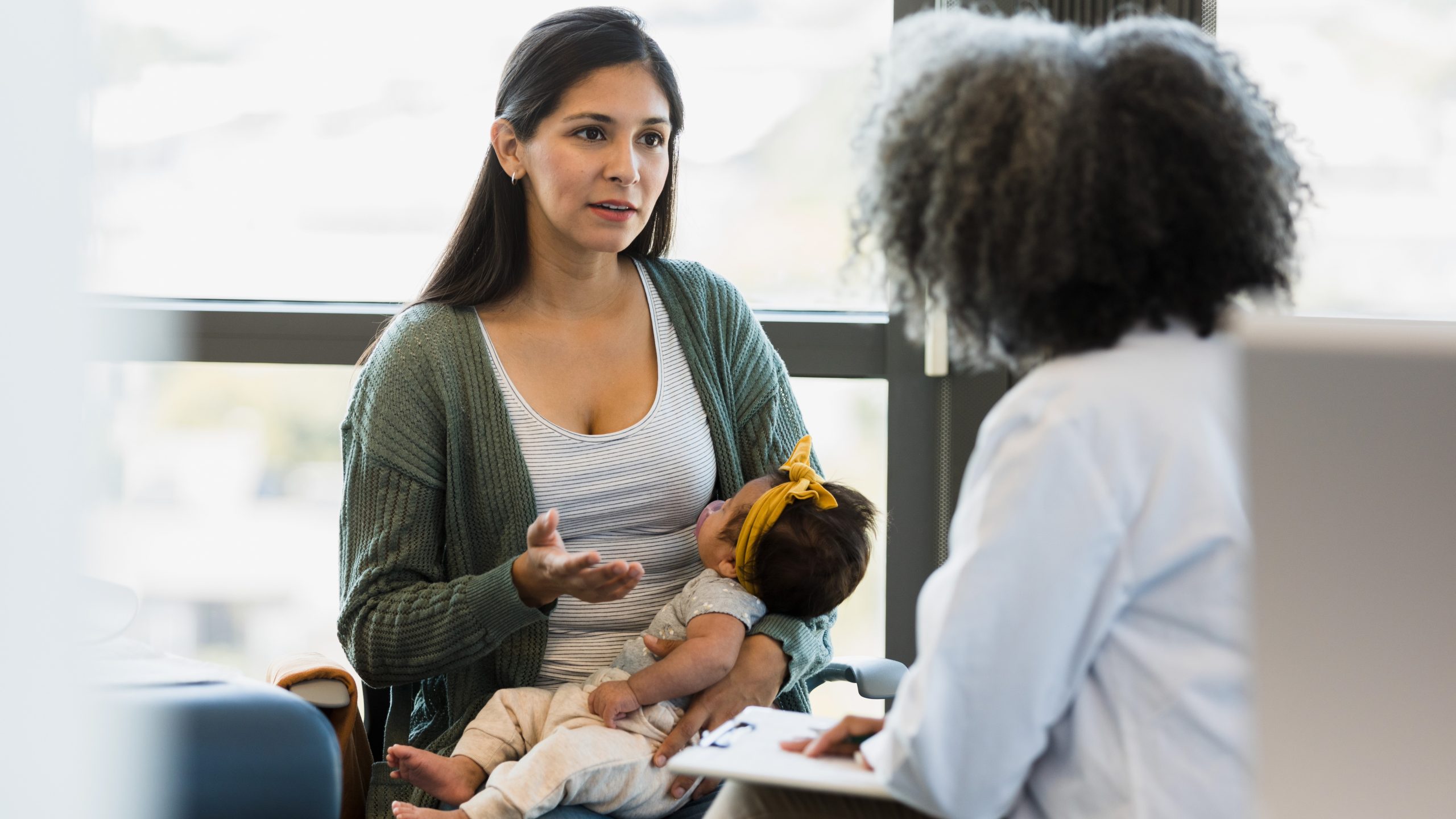 — title missing — Woman holding a baby and talking to a healthcare provider in a doctor's office