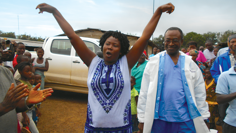 Joyful Survivor A joyful woman with arms raised celebrates with a doctor and community members in the background.