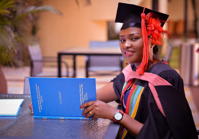 WFETP South Africa A woman wearing a black cap and gown with red accents is smiling while holding a blue book.