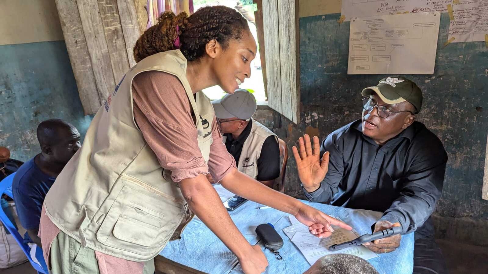 Mpox vaccine trial_DRC CDC staff prepare for a vaccine trial. Multiple individuals are sitting around a table while one woman talks with a man holding a tablet.