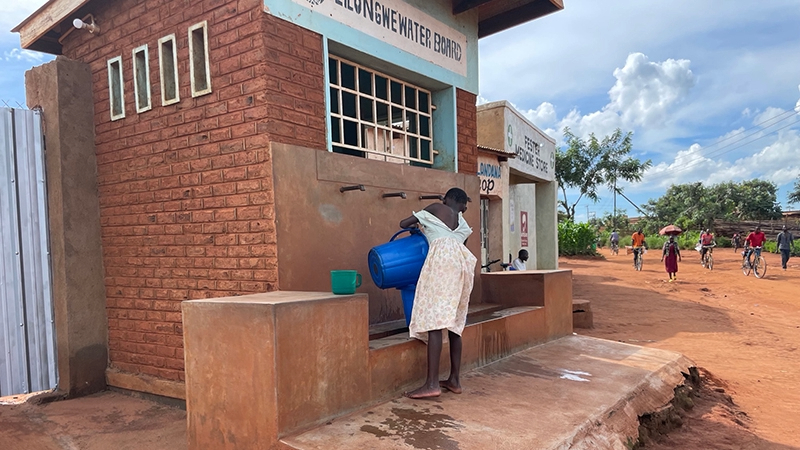 Cholera-Malawi-Andrea-Martinsen-Feb-2023_16x9 A person holds a bucket while standing in front of an outdoor water station