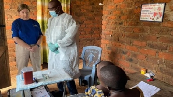 — title missing — CDC Alison Johnson wearing a blue shit and beige pants and a man in a lab coat monitor field staff conducting an interview in a household in Tanzania.