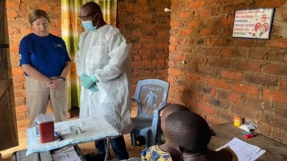-- title missing -- CDC Alison Johnson wearing a blue shit and beige pants and a man in a lab coat monitor field staff conducting an interview in a household in Tanzania.
