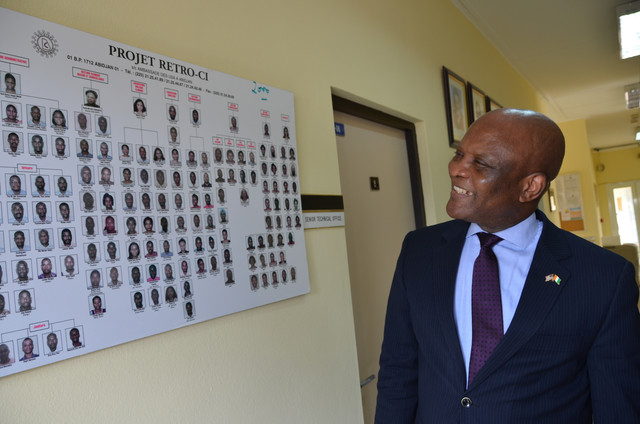 2023_SuccessStory_RetroCI Dr. John Nkengasong stands in a hallway smiling while looking at a poster of individuals working for Project Retro-CI.
