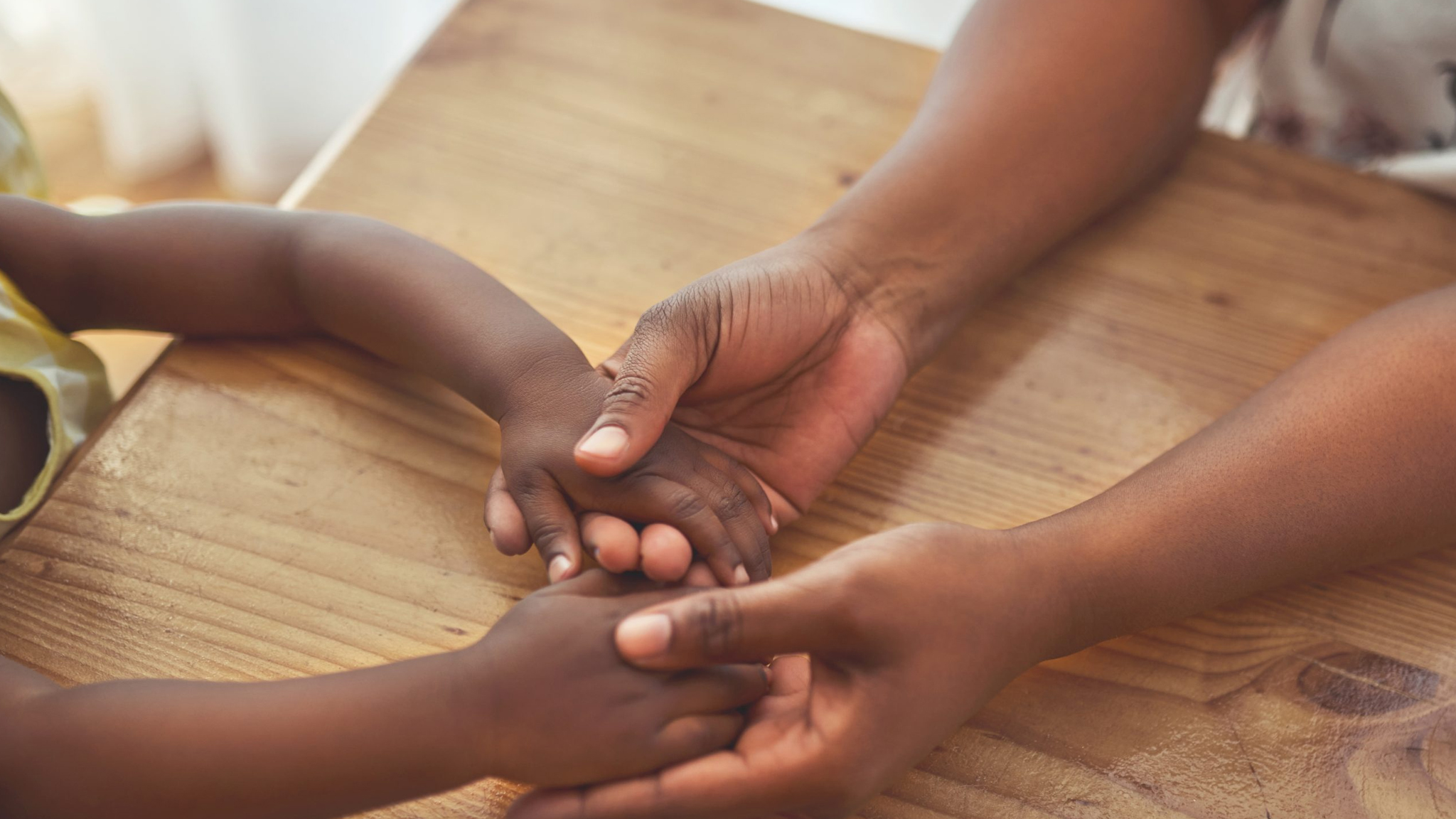 OVC_DRC_2024 An adult holds the hands of a child at a table.