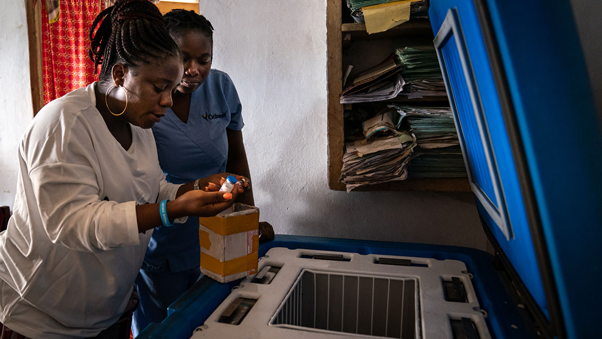 Two health care workers check vaccines in a storage refigerator.