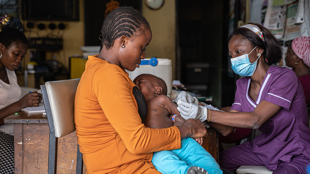 A mother in Nigeria gets her son vaccinated. A mother holds her young son as a health worker gives a vaccine to the child.