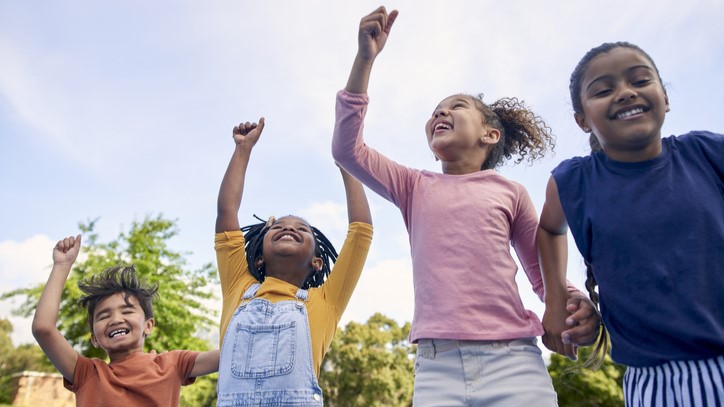 Four children playing outside Four children playing outside with hands raised to the sky.