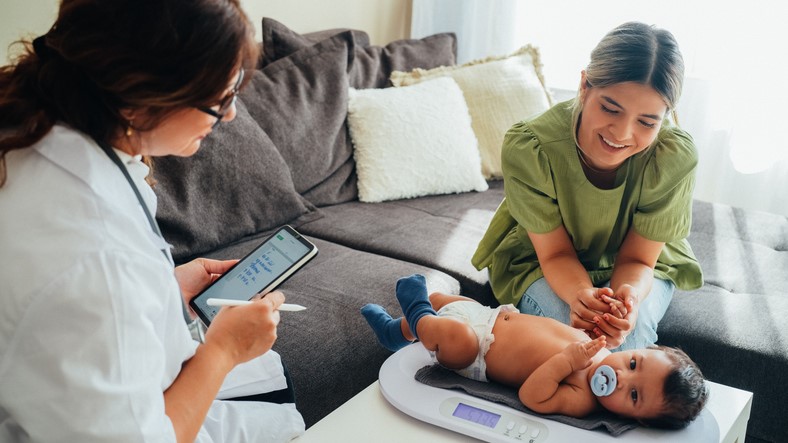 Health care provider, mom, and baby Baby on scale with health care provider and mother nearby .