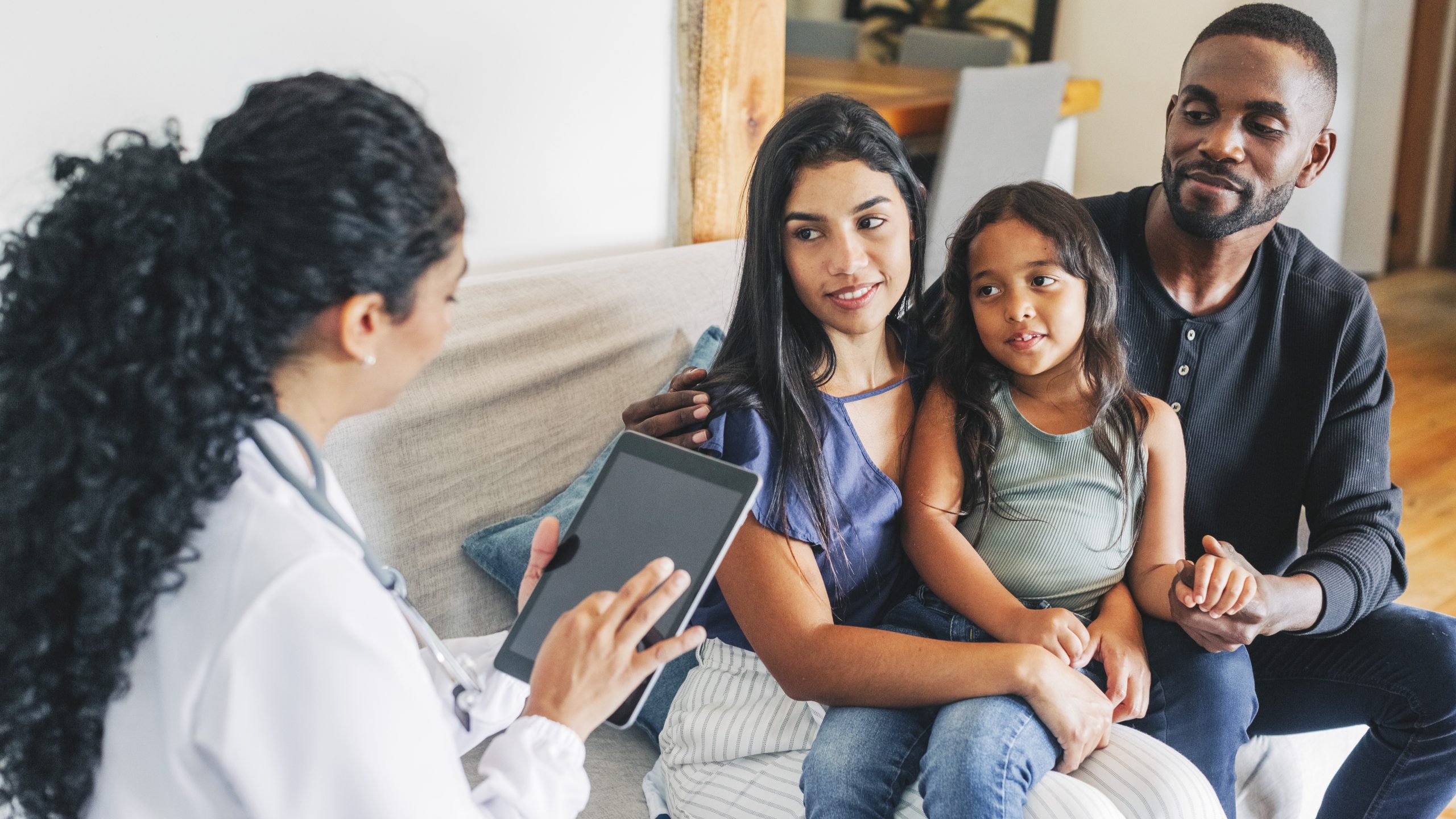 Family medical consult Health care provider holding a tablet and talking with a family of parents and their child.
