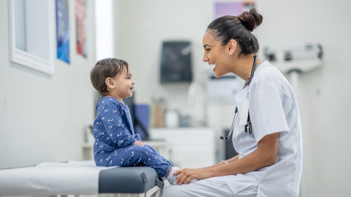 Toddler at checkup Toddler sitting on exam table and laughing with health care provider.
