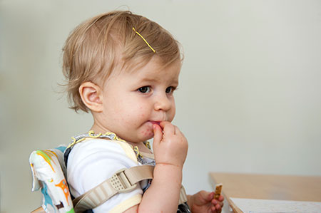 toddler-eating Niña pequeña con puntos rojos alrededor de la boca, comiendo en una mesa.