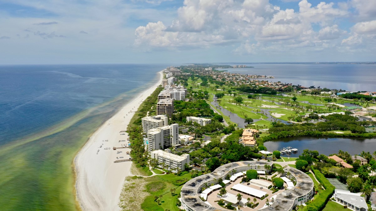 Aerial view of bloom near beach Aerial view of a beach with nearby hotels, other buildings, and a golf course. The water along the beach is murky and green, but clear farther from the shore.