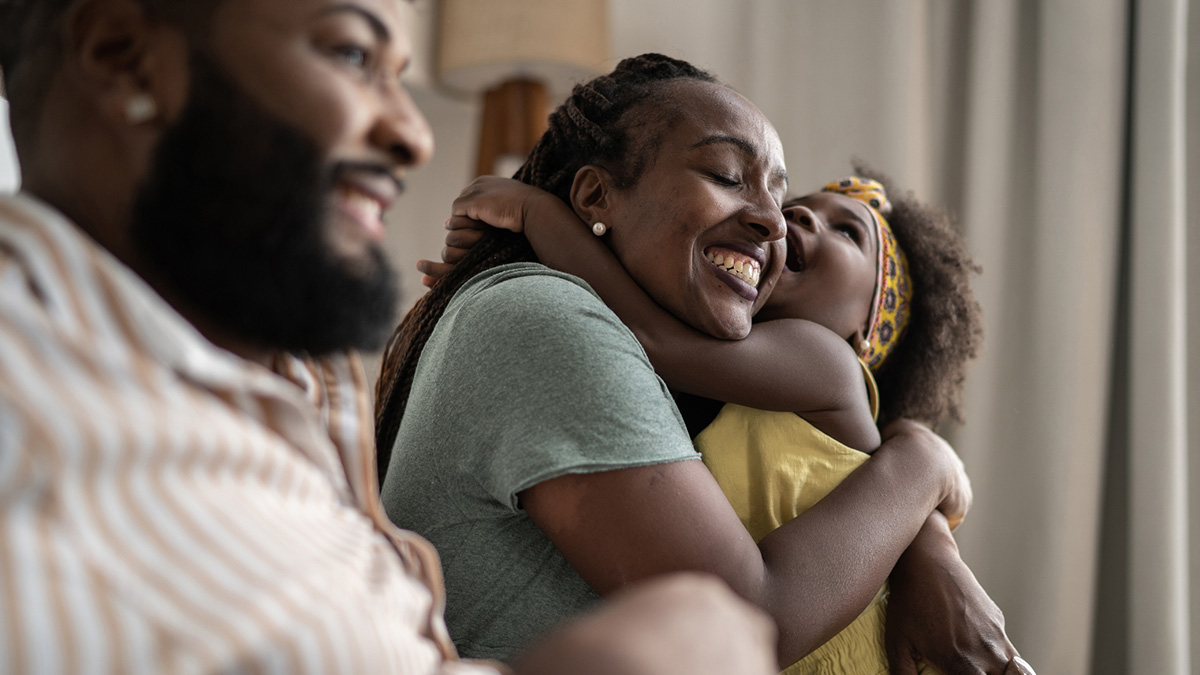 Happy and healthy Black family A man, woman, and child share hugs and laughs.