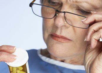 older-adults-pill-bottle.jpg Woman reading sticker on pill bottle.
