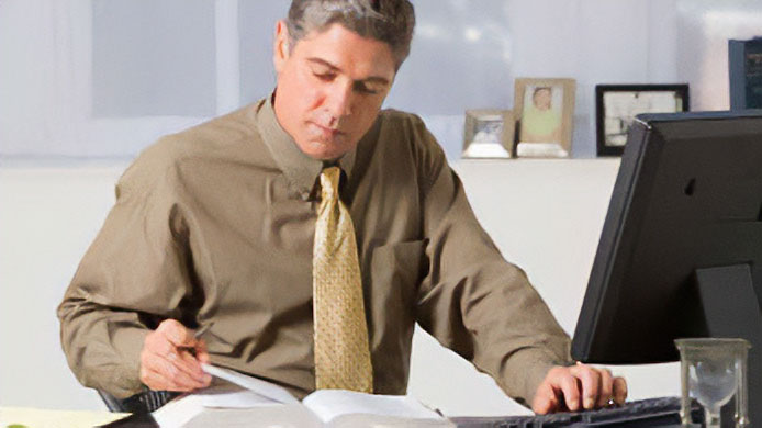 Man reading book and using computer Man looking at a book while typing on a keyboard.