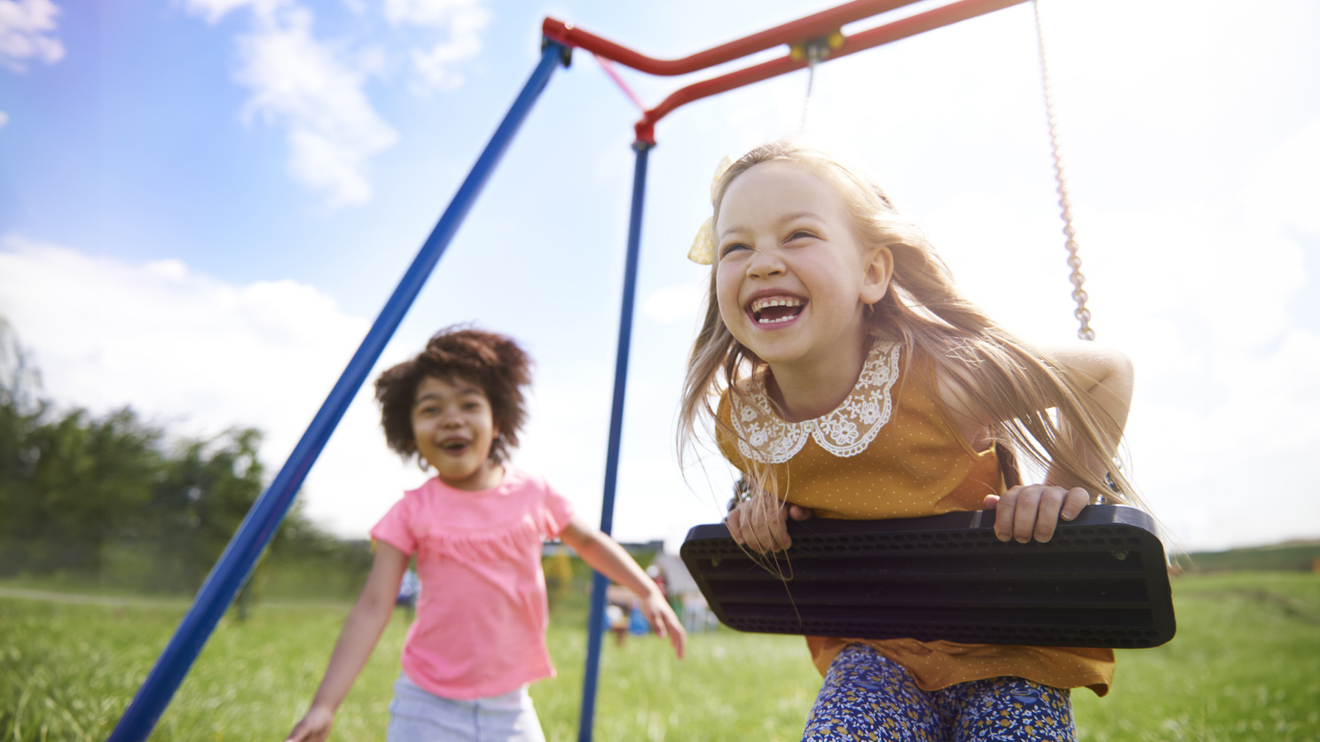 The best friends playing together Child on a swing with another child approaching the swings.