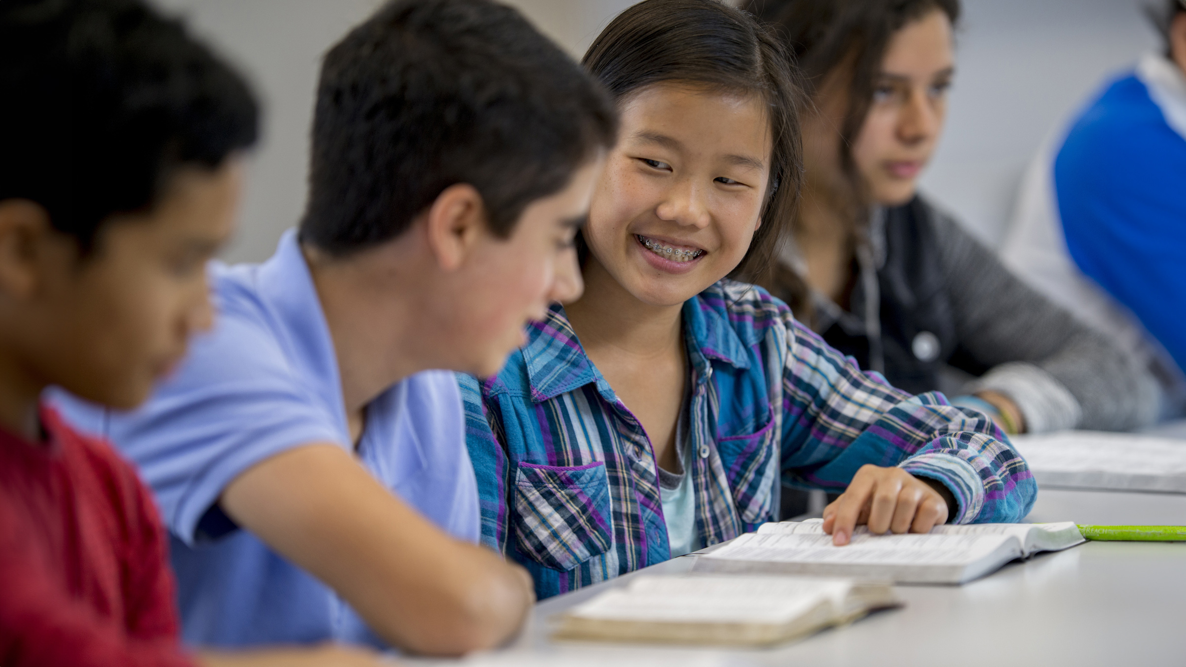 Working on a Group Assignment Together Four students at a table, open books in front of them. Two students in the middle are talking to each other.