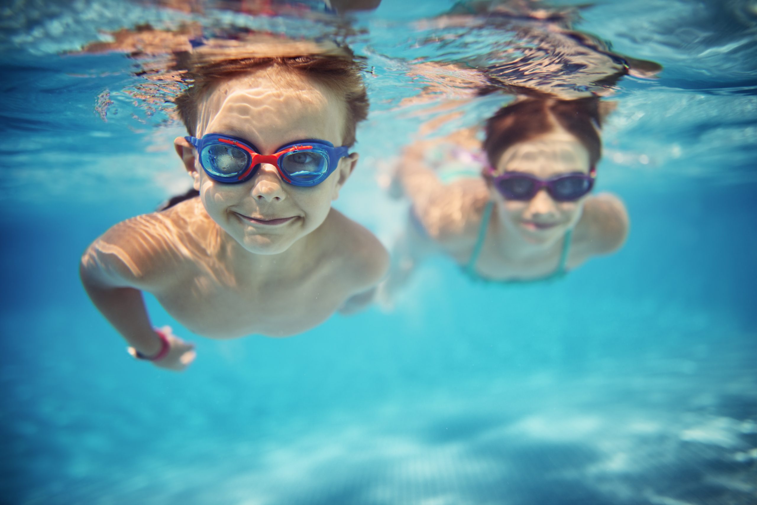 Two boys swimming under water Two youn.g boys swimming in a pool under water wearing goggles