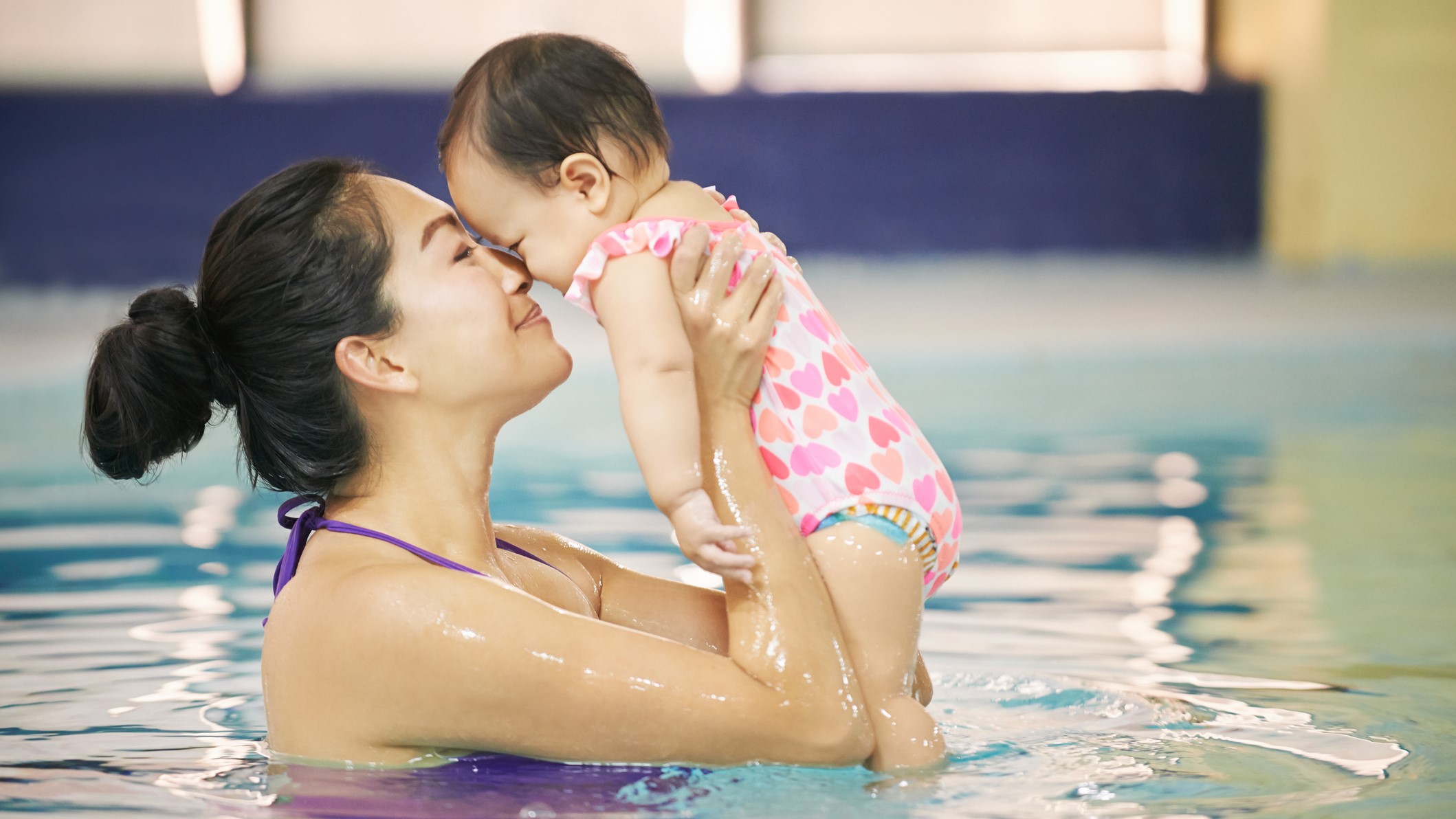 mother and baby in pool Madre en una piscina sosteniendo a un bebé que está usando un pañal para nadar.