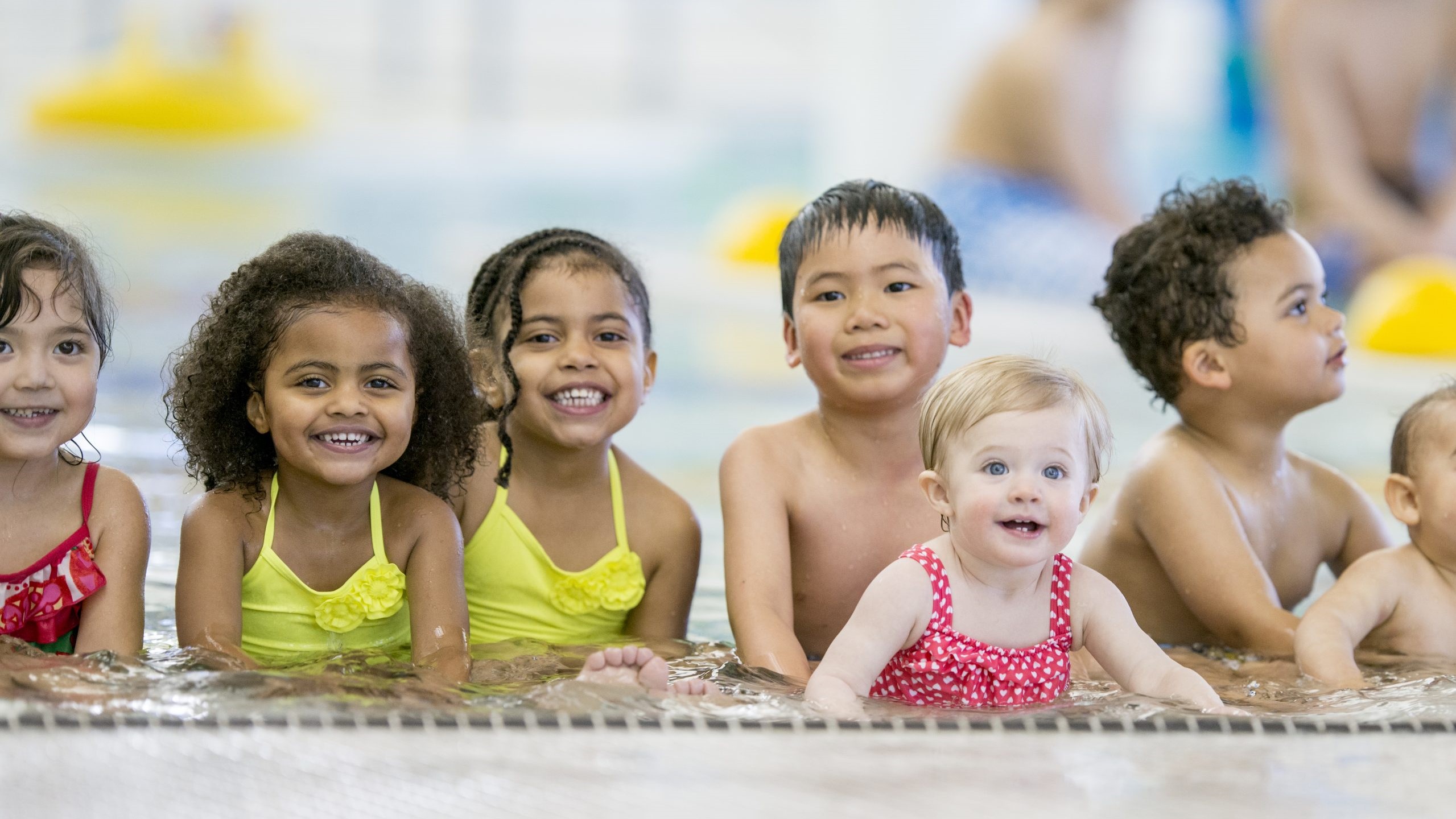 — title missing — Young kids sitting in the shallow end of the pool together.