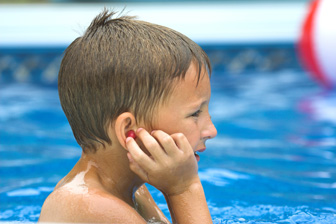 swimming boy touching his ear Niño en la piscina poniéndose tapones para los oídos.