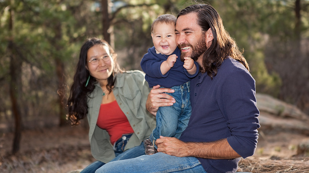 Healthy Tribes Young Family Young American Indian family with mom, dad, and toddler sitting on a rock in the woods.