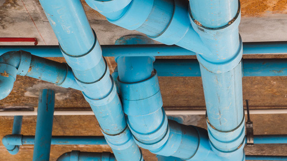 Blue pipes running in different directions at the top of an unfinished ceiling inside a building.