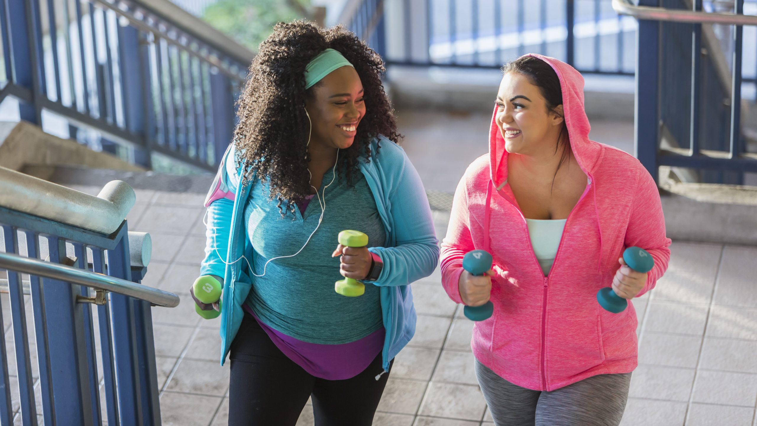 — title missing — Two women walking up stairs while carrying hand weights.