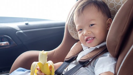 — title missing — Boy in car seat eating a banana.