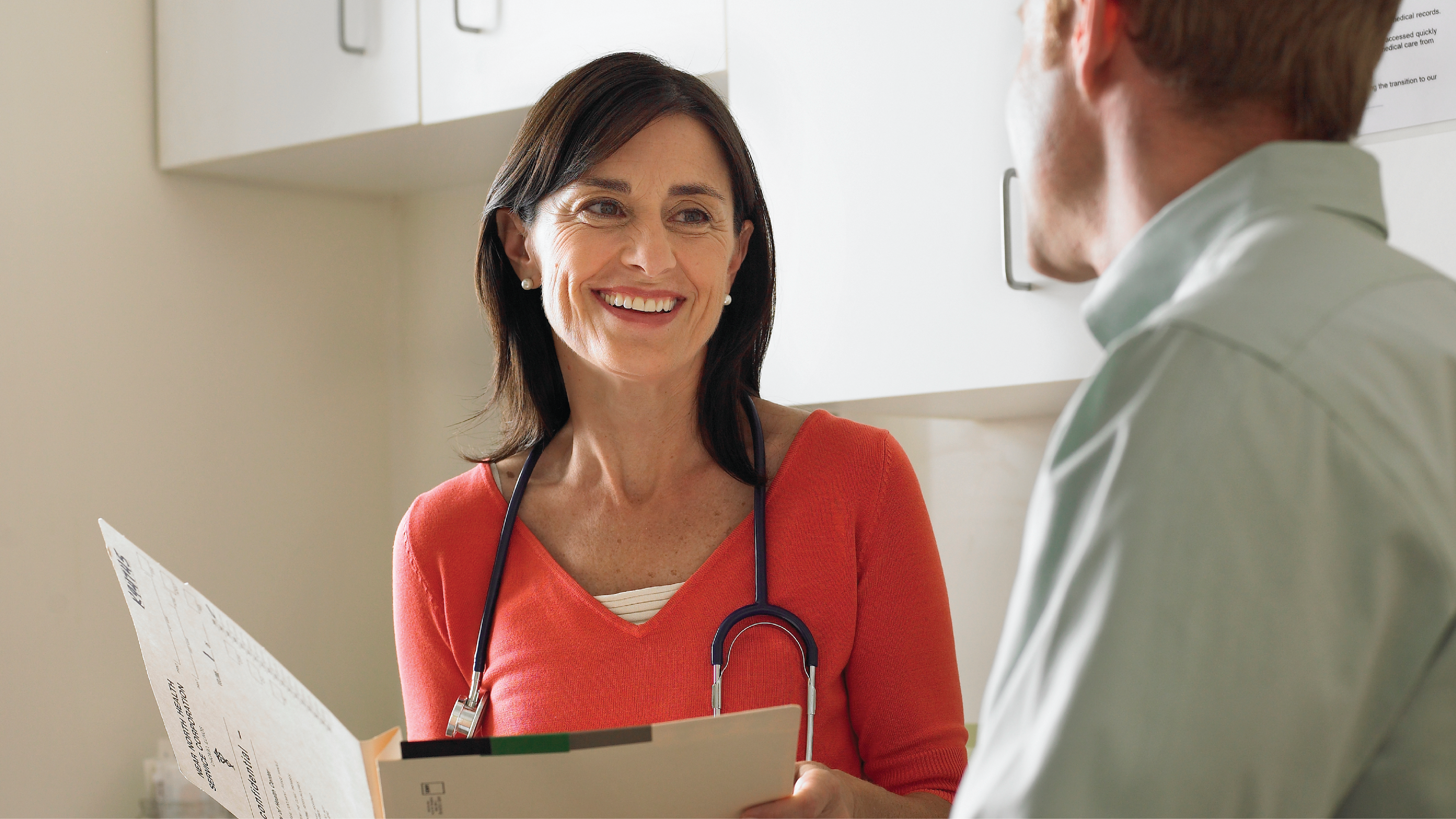 Testing Thumbnail A health care provider smiling and holding a medical chart while talking to a patient.