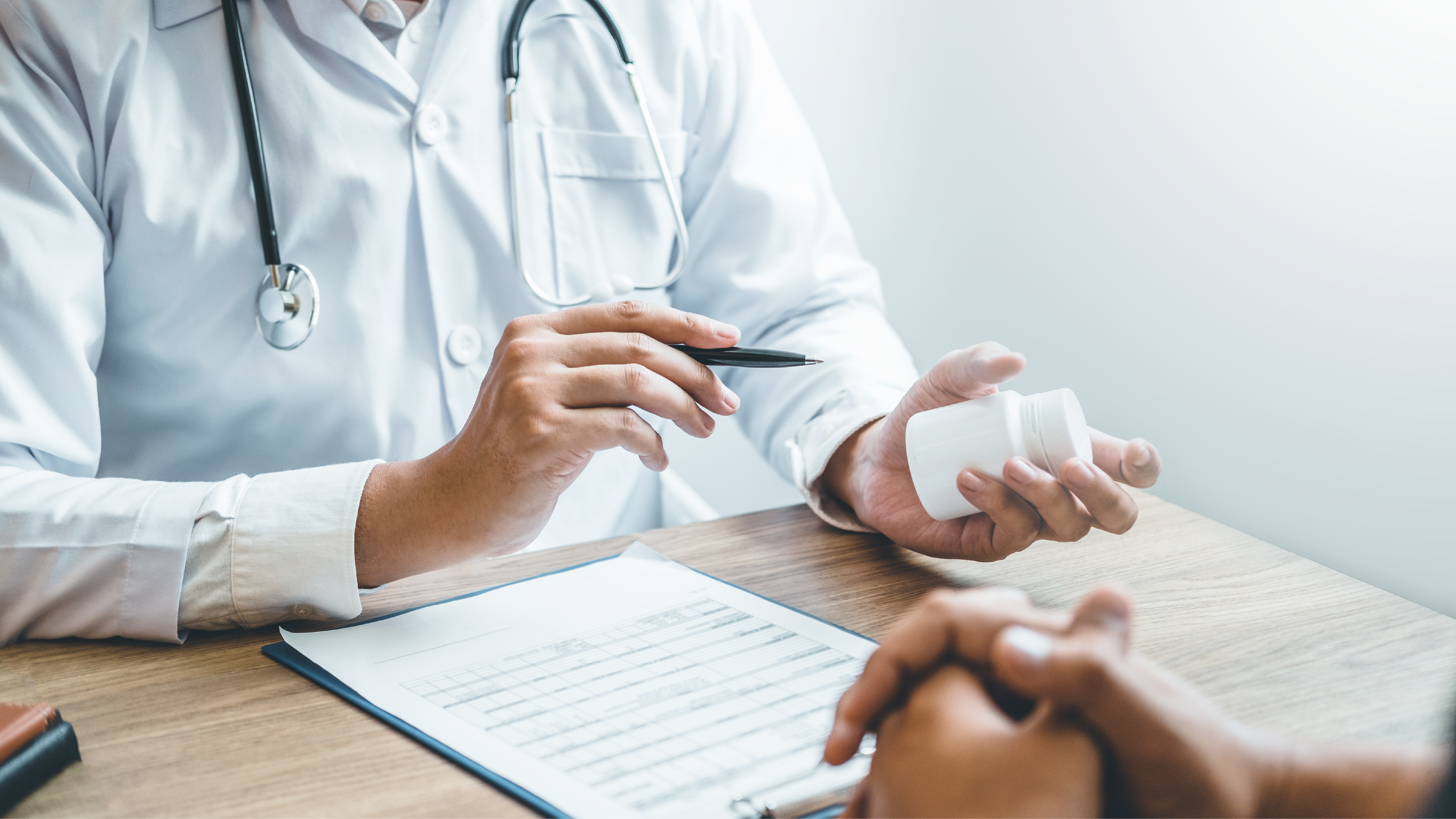Thumbnail for PrEP A health care provider’s hands and body, sitting at a table facing a patient, holding and pointing to a pill bottle.