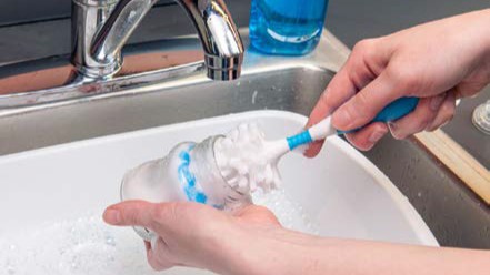 clean-feeding-items-3a A person washing a bottle with a scrub brush.