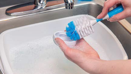 clean-feeding-items-3b A person cleaning bottle cap with scrub brush.