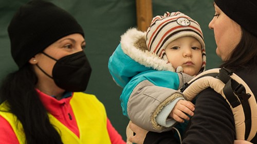 — title missing — A relief worker assisting a mother and her baby during an emergency.