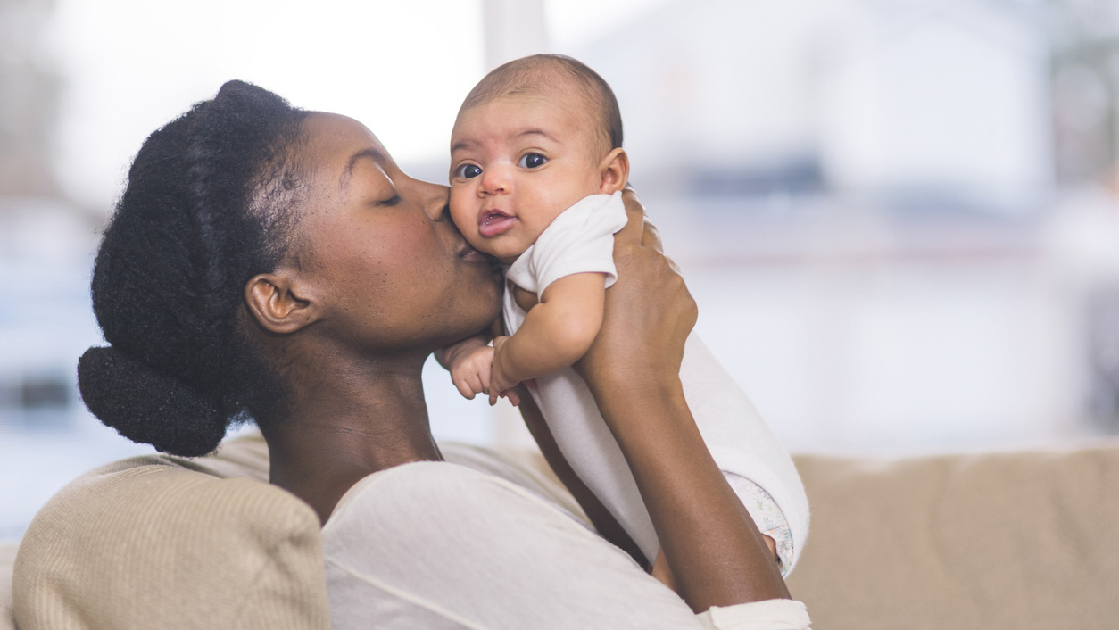 Full sign - birth to 5 months A mother kissing her child.
