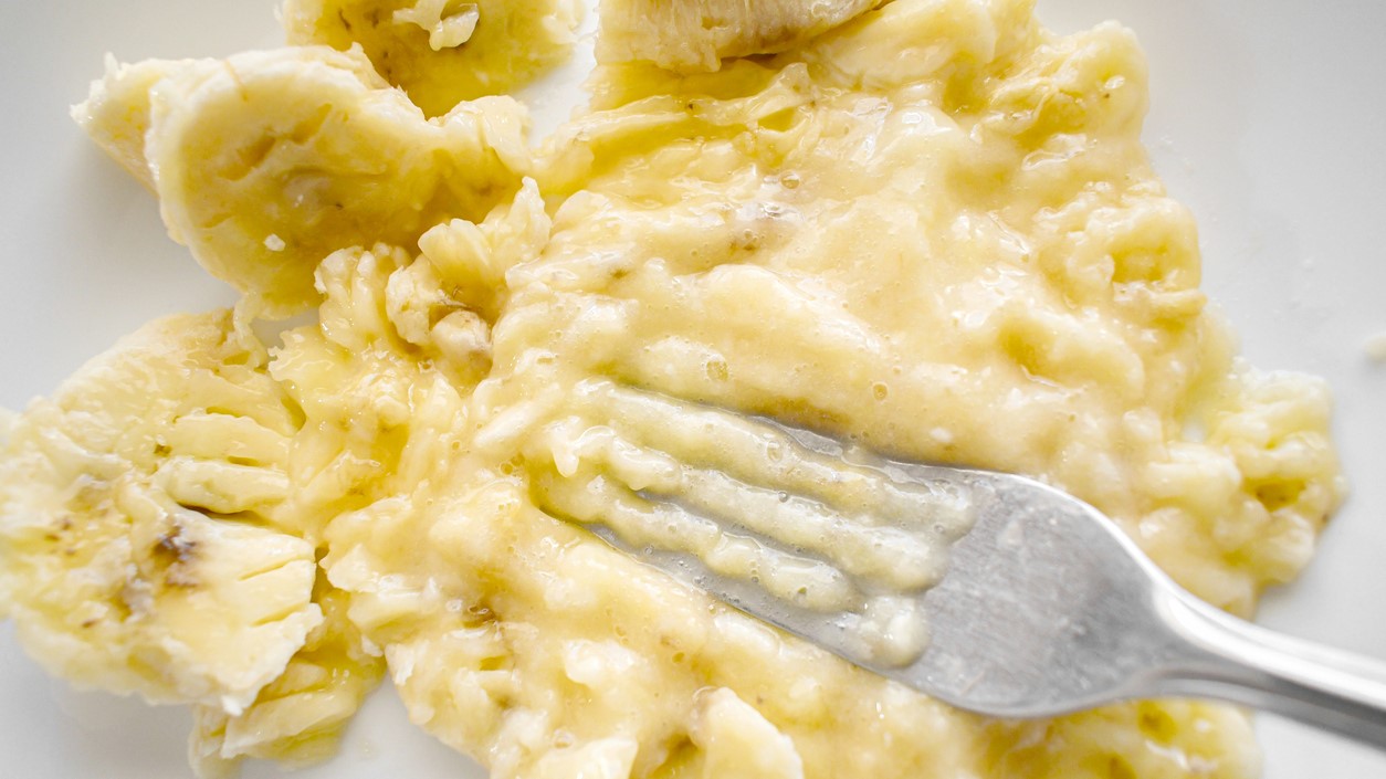 mashed banana Ripe banana being mashed with a fork on a white plate.