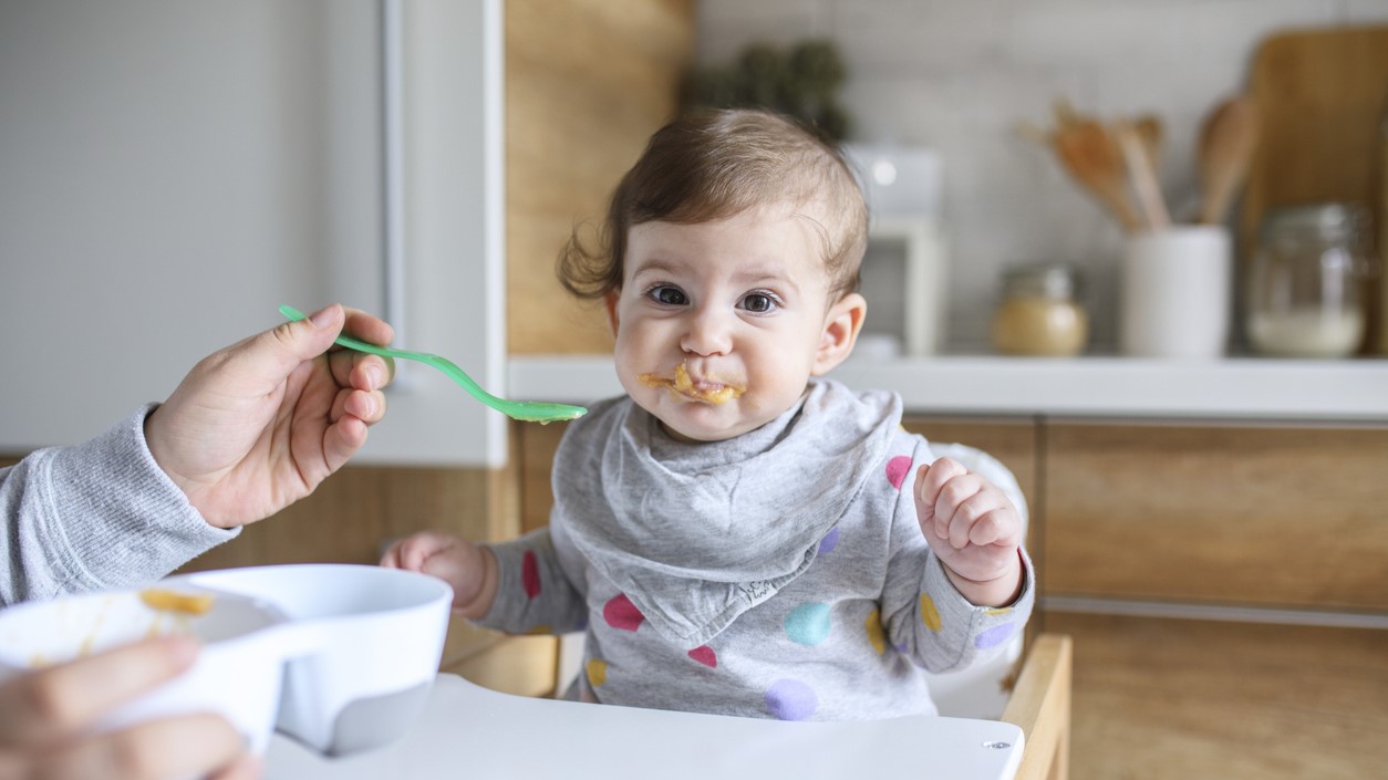 Baby fed in highchair Parent feeding baby with a spoon.