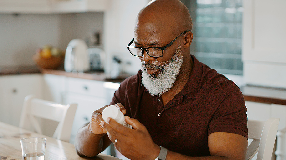 IBD Senior Man Reading Medicine Bottle Senior African American man with bald head, white beard and glasses reading medicine bottle.